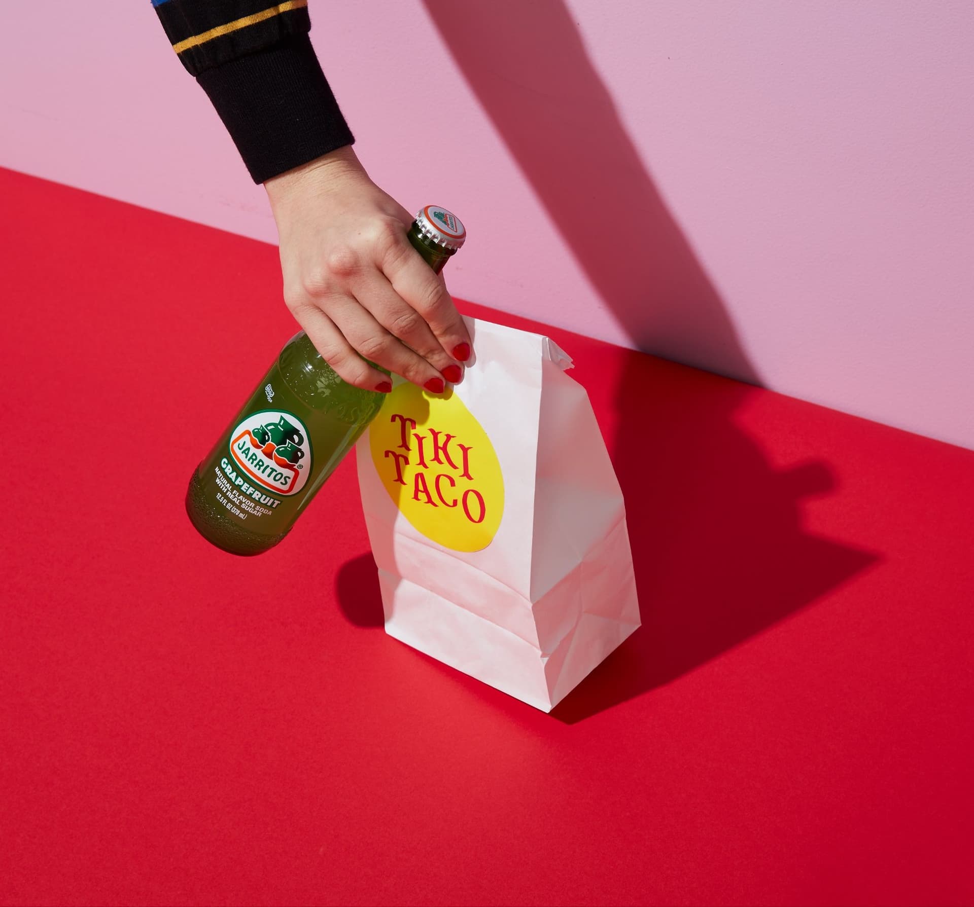 A person holding a soda and a bag that says Tiki Taco