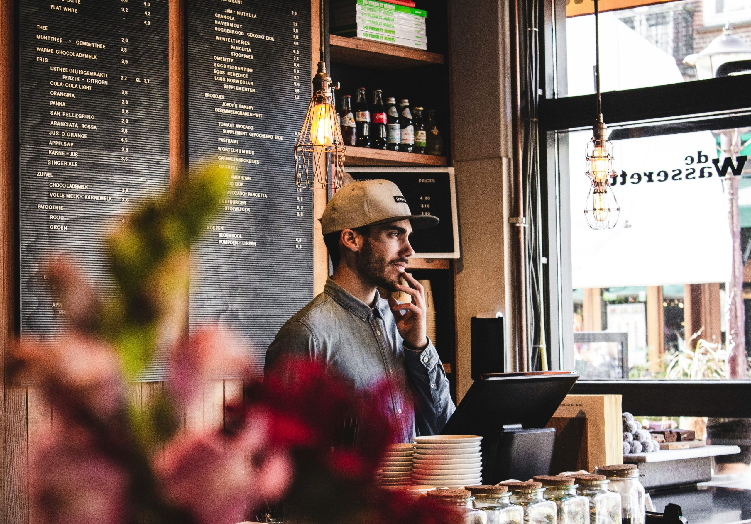 A man standing, working at a restaurant staring out of the window.